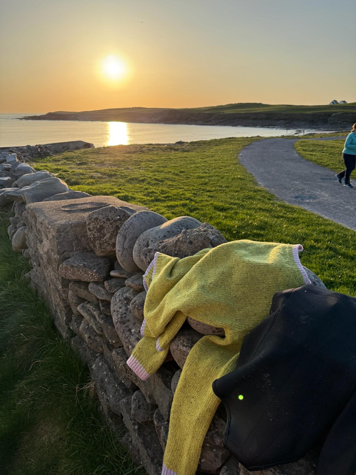 Wild Meadows Green Aoife Mc Namara Jumper draped over stone wall in County Clare at sunset
